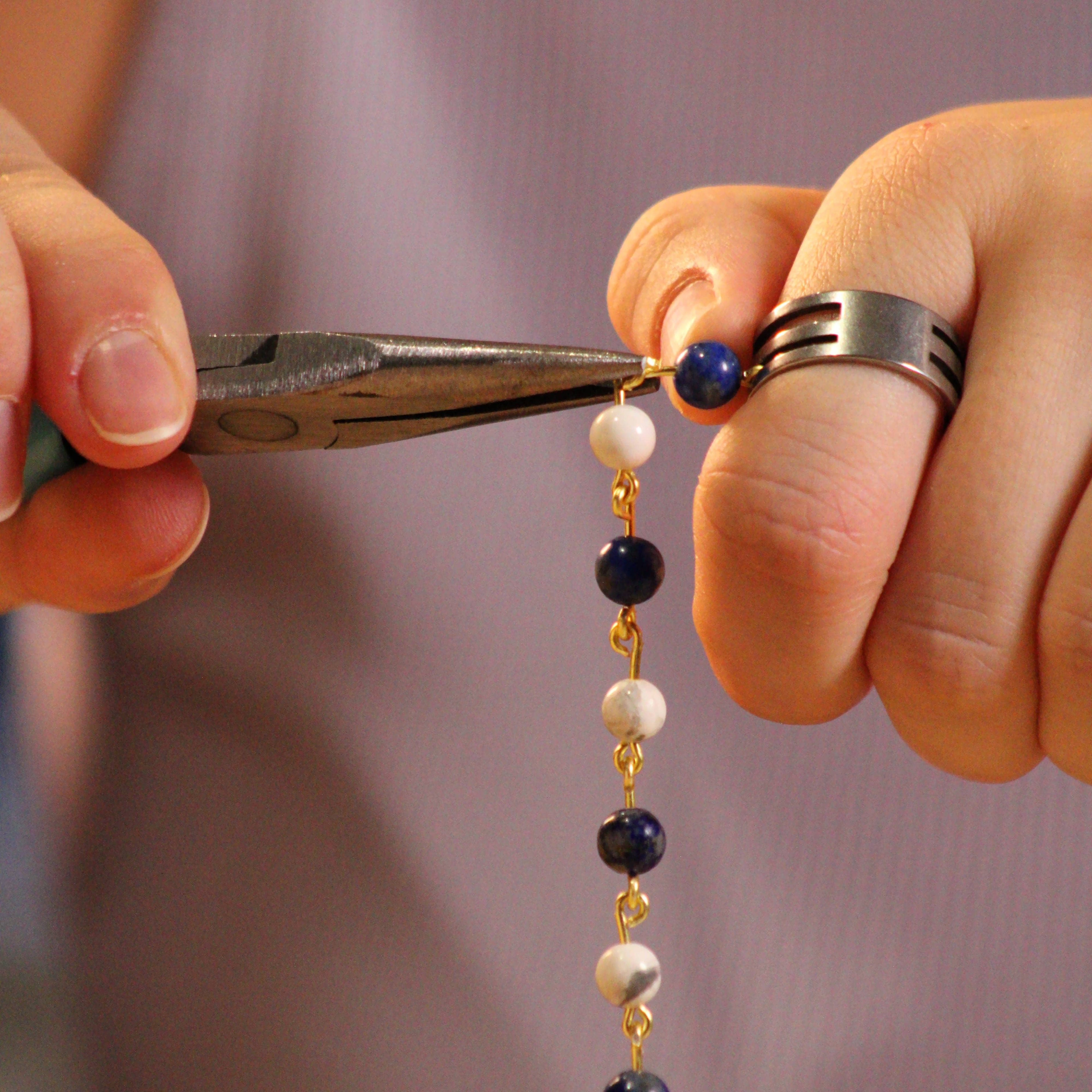 photo de la fabrication d'un bracelet avec une pince serrant les anneaux de jonctions entre les perles