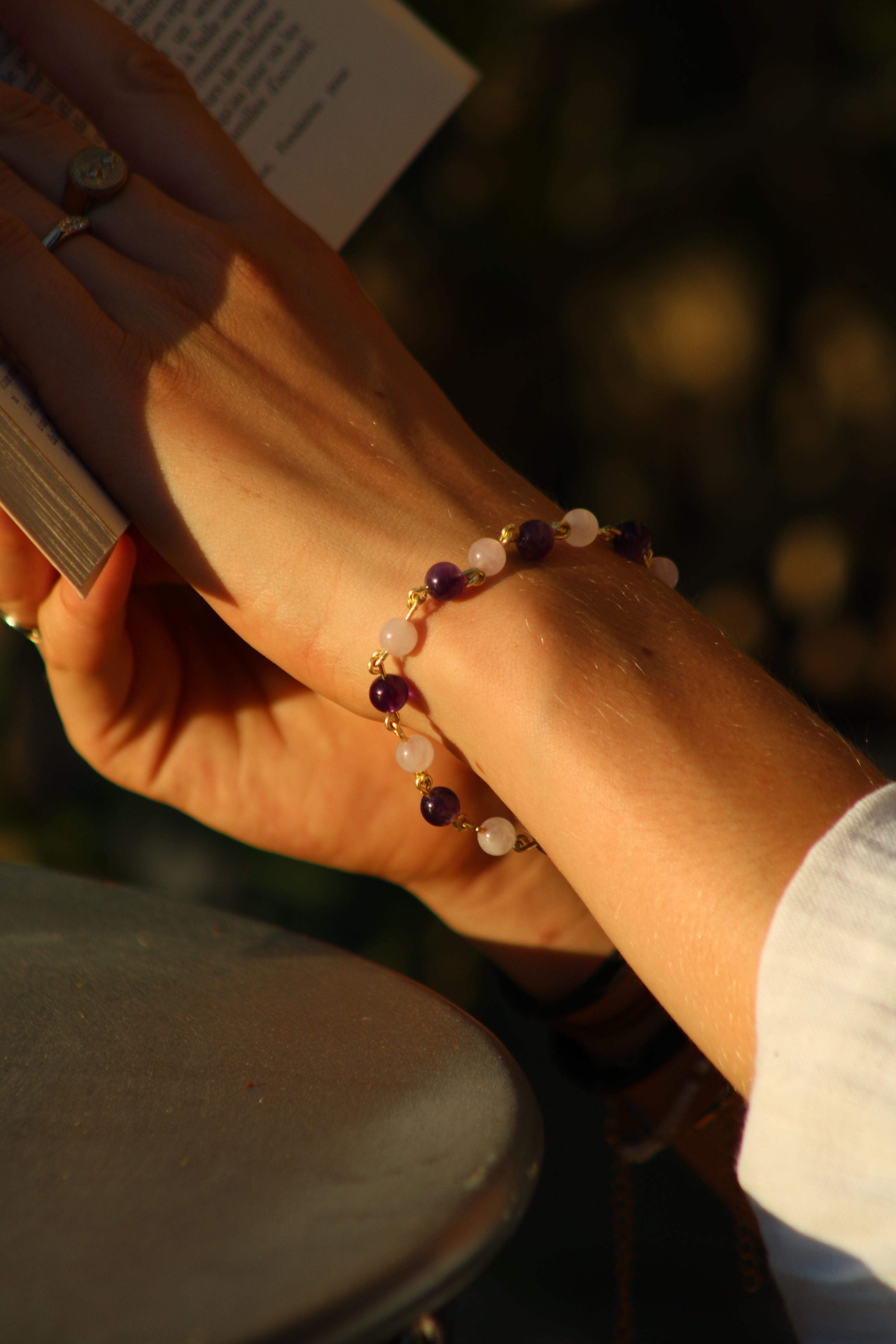 photo d'une femme tenant un livre avec un bracelet Ornéa composé de pierres naturelles d'amethyste et de quartz rose, bracelet finition or