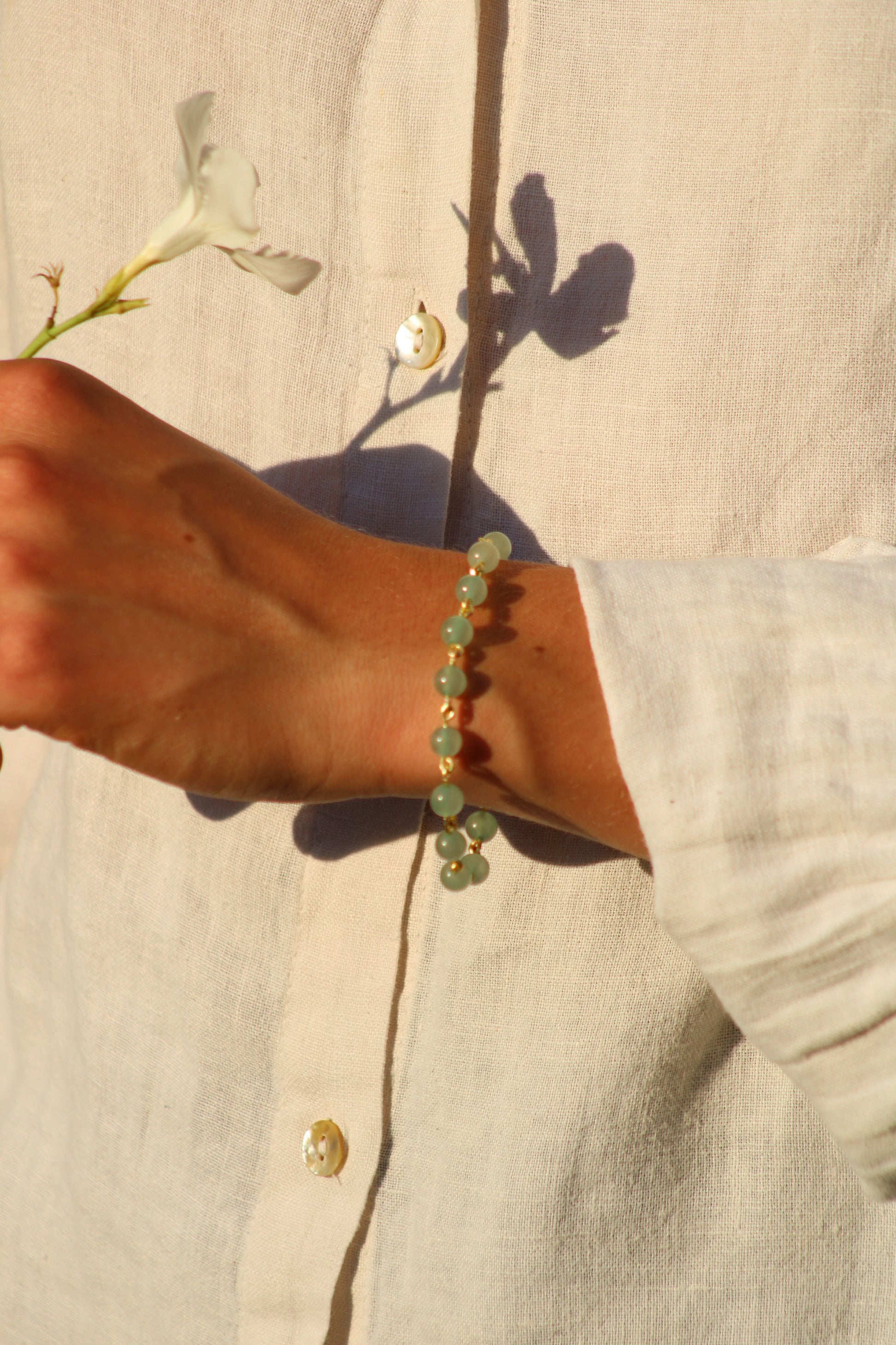 photo du bracelet Ornéa en perles d'aventurine, finition or, porté par une femme tenant une fleur blanche dans la main